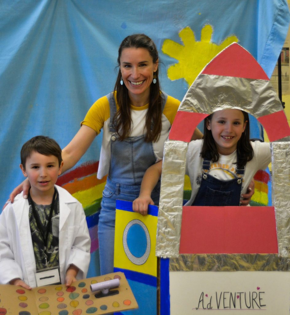 Kristine St-Pierre and her two young colleagues performing a children's show, one in a cardboard and tinfoil rocket, and the other is a NASA control room operator!  Kristine has her hands on their backs as they all pose for the photo